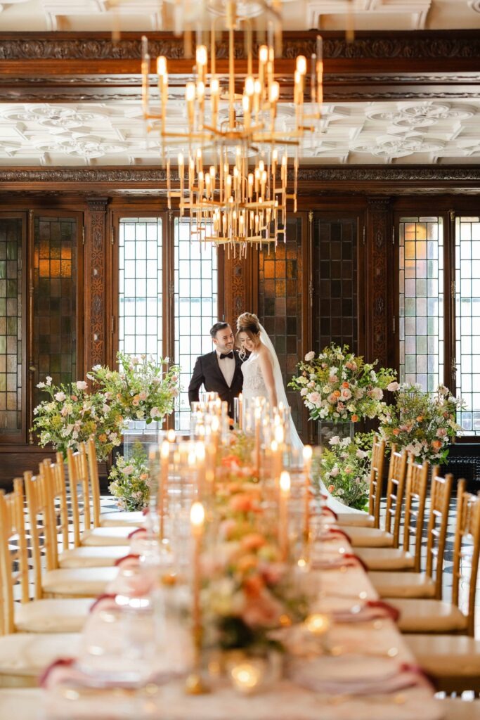 A bride and groom pose elegantly standing at the head of a reception table under gold chandeliers at their Blackstone Hotel Chicago wedding