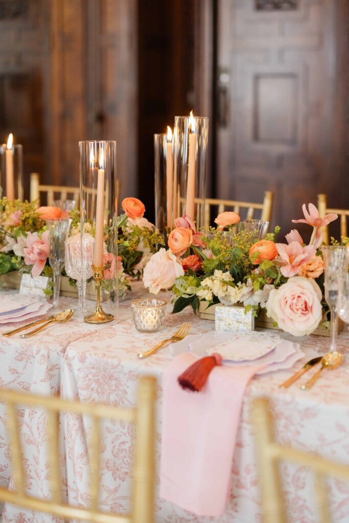 An elegant tablescape with a pastel pink floral tablecloth, lush pink flowers, and peach candles at a Blackstone Hotel Chicago wedding
