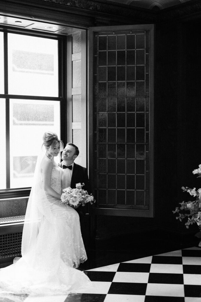 A black and white photo of a bride and groom sitting on a windowsill at their Blackstone Hotel Chicago wedding
