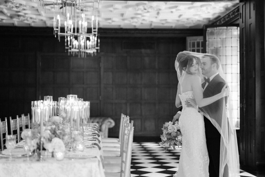 Black and white photo of a bride and groom inside the bride's veil next to a reception table at a Blackstone Hotel Chicago wedding