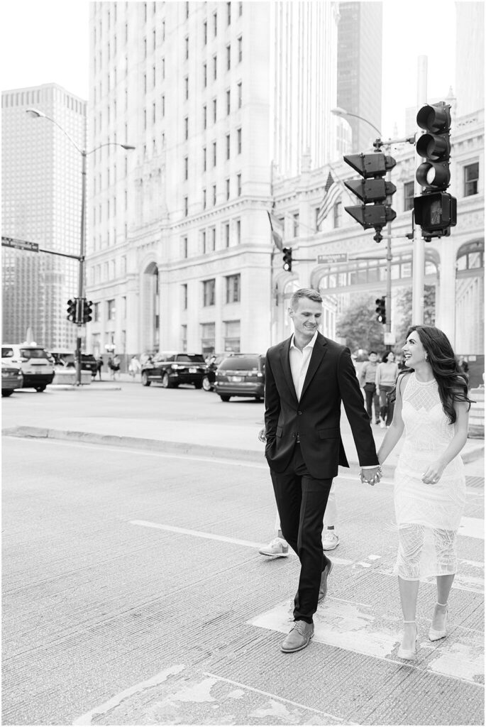 Black and white engagement photo of a man and woman holding hands while walking down a downtown Chicago street.