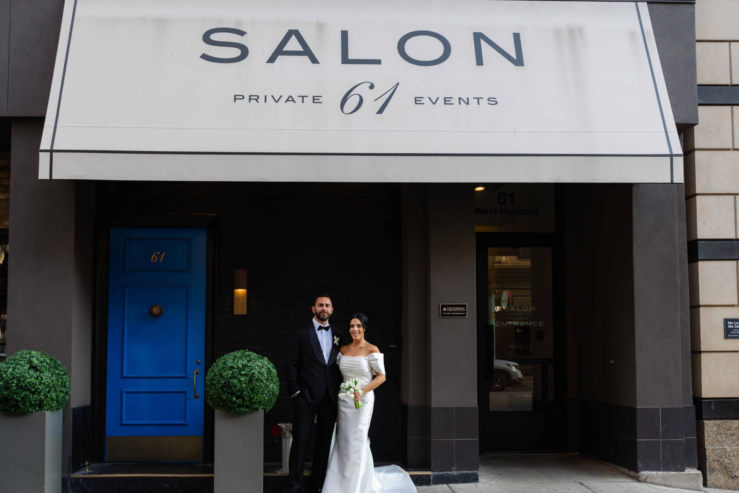 Bride and groom pose beneath the Salon 61 Private Events awning outside the Chicago wedding venue.